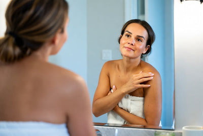 Woman in a towel looking at herself in the mirror, applying Sol Rx balm.